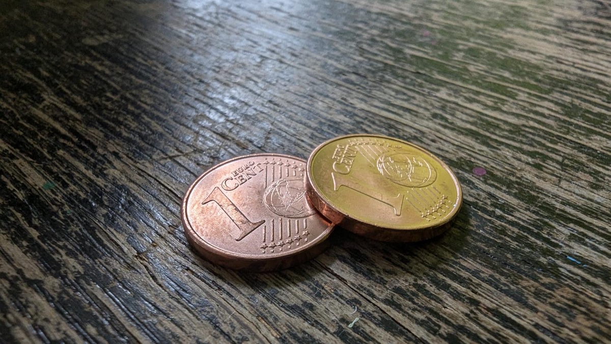 Eine Cent- und eine Zwei-Euro-Münze liegen auf einem Holztisch.
